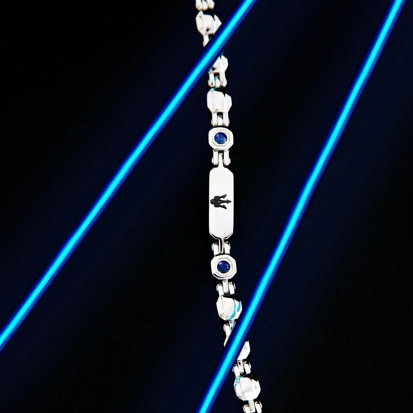 Ανδρικό βραχιόλι ταυτότητα Maserati JM335AXO12 ατσάλινο σε ασημί χρώμα με μαύρη τρίαινα και μπλε ζιργκόν πέτρες σε μαύρο φόντο.