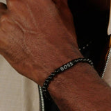 Ανδρικό βραχιόλι Boss 1580659M με μαύρες χάντρες, διακοσμημένο με μαύρο κυλινδρικό στοιχείο από ανοξείδωτο ατσάλι., φορεμένο.