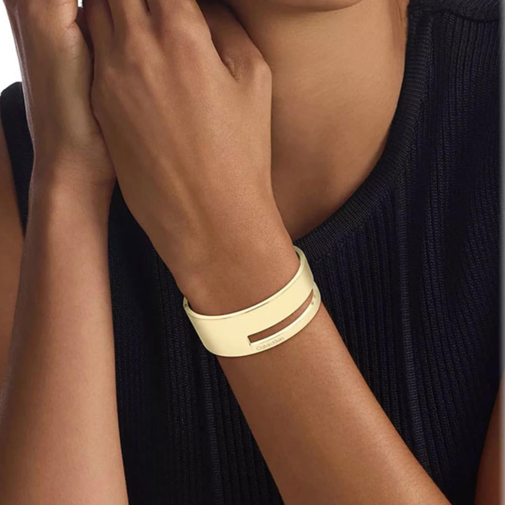 Γυναικεία χειροπέδα Calvin Klein 35000673 σε χρυσό χρώμα από ανοξείδωτο ατσάλι με στοιχεία από το λογότυπο της εταιρίας, φορεμένη