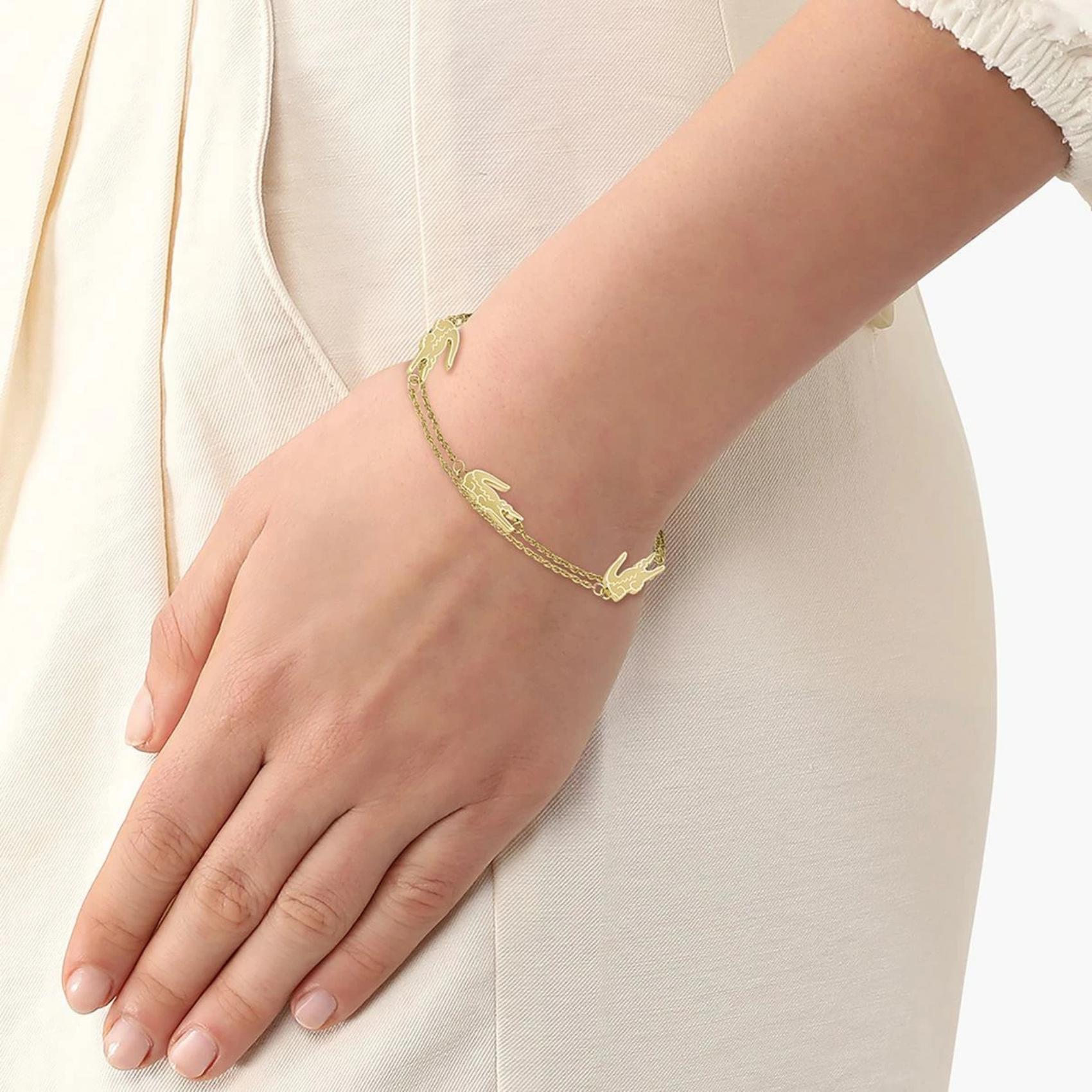 Γυναικείο βραχιόλι Lacoste 2040470 ατσάλινο σε χρυσό χρώμα από ανοξείδωτο ατσάλι με στοιχεία από το λογότυπο της εταιρίας, φορεμένο.