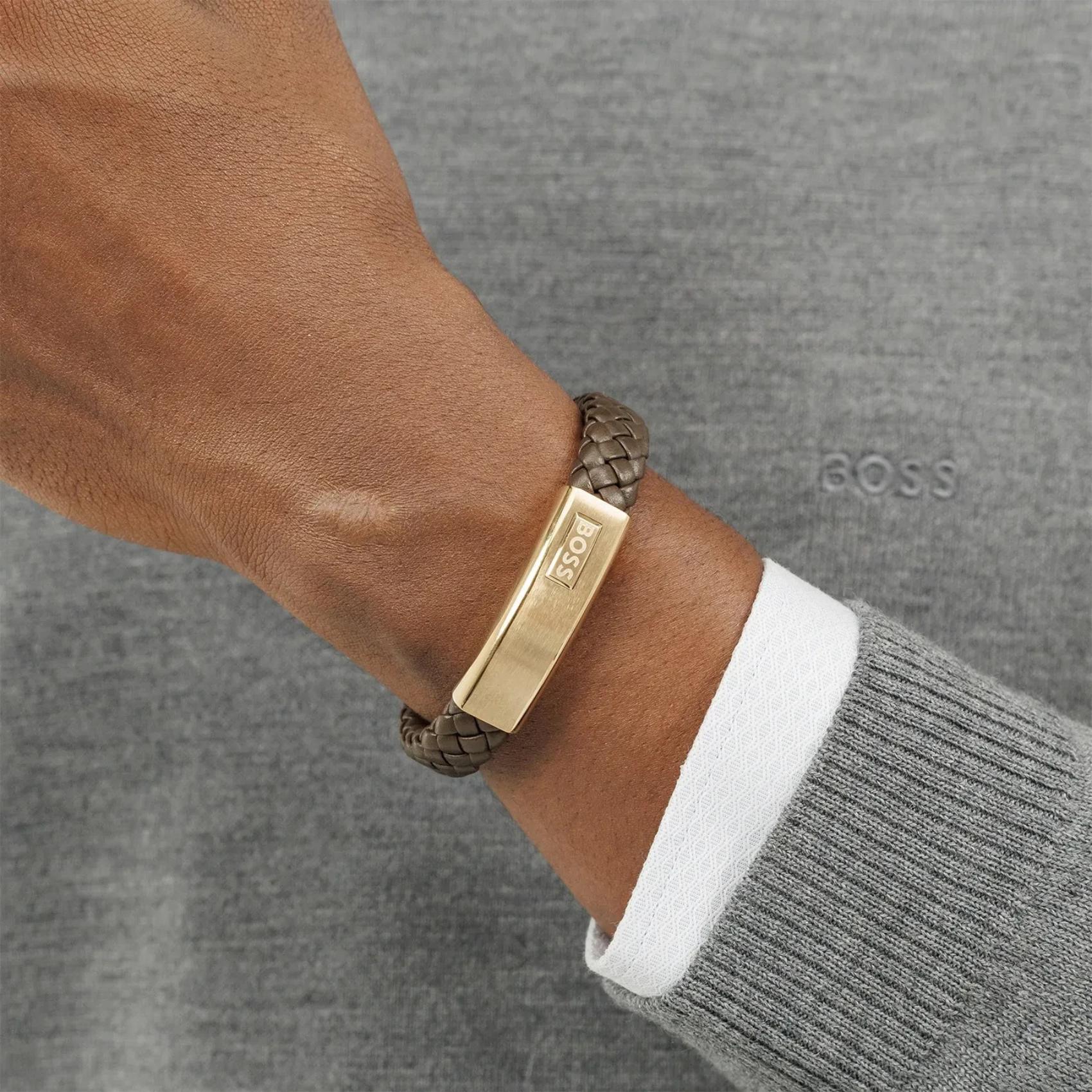 Ανδρικό δερμάτινο βραχιόλι Boss 1580746M σε καφέ χρώμα με πλεκτό σχέδιο και χρυσή ταυτότητα, φορεμένο.