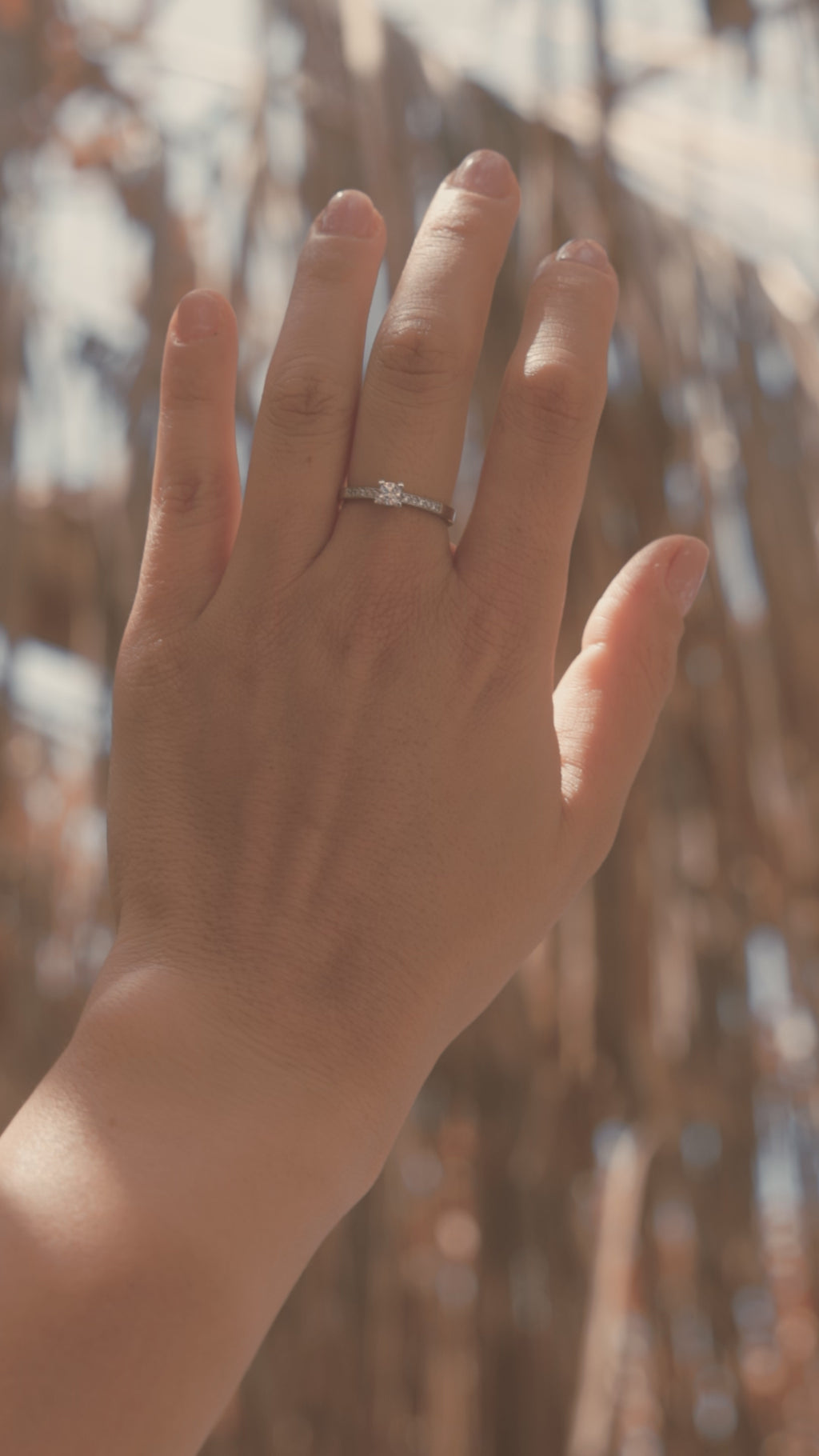 Mονόπετρο δαχτυλίδι με διαμάντι κατασκευασμένο από λευκόχρυσο με καστόνι σχήματος "V" και πλαϊνές πέτρες από μικρότερα διαμάντια, φορεμένο σε γυναικείο χέρι.
