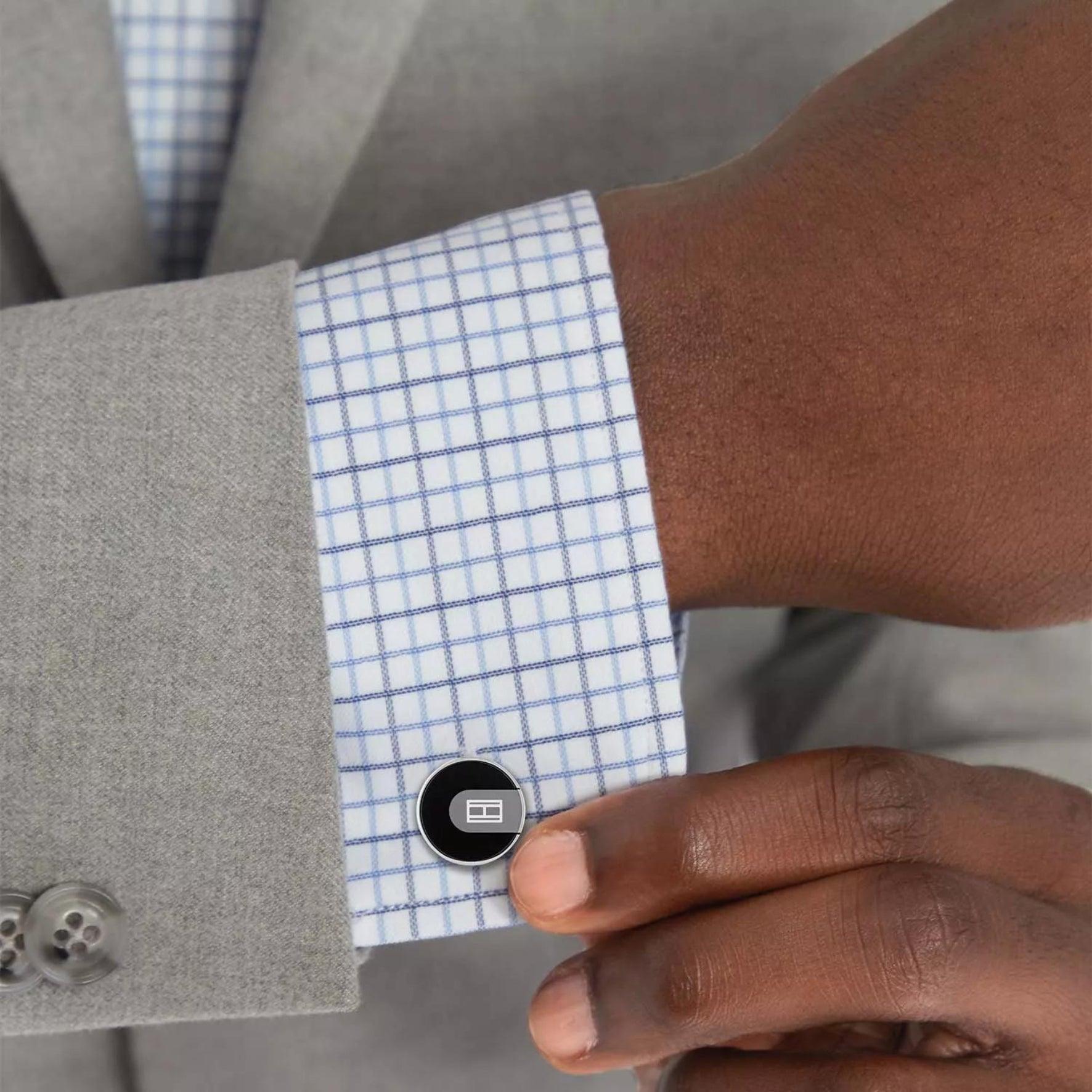 Ανδρικά μανικετόκουμπα Tommy Hilfiger σε ασημένιο χρώμα στρογγυλό σχήμα και μαύρο σμάλτο κατασκευασμένα από χειρουργικό ατσάλι φορεμένα με πουκάμισο σε ανδρικό χέρι.