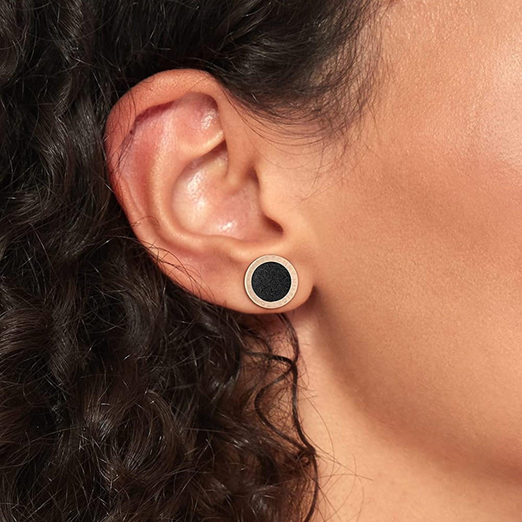 Γυναικεία σκουλαρίκια καρφωτά Tommy Hilfiger με στρογγυλό σχέδιο σε ροζ χρώμα και μαύρο εσωτερικό φορεμένα σε γυναικείο αυτί.