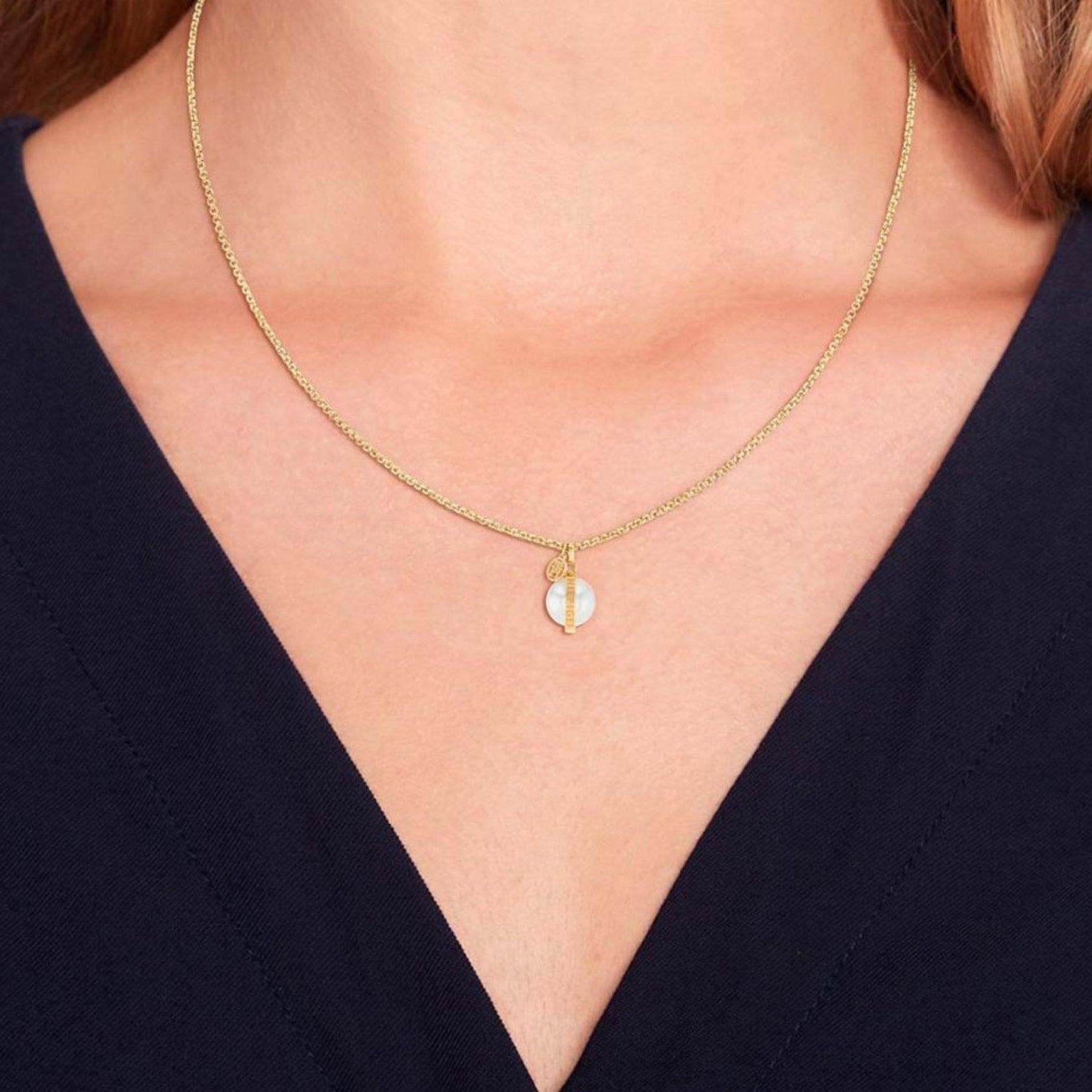 Γυναικείο κολιέ Tommy Hilfiger σε χρυσό χρώμα, με στρογγυλό μοτίφ από λευκό φίλντισι φορεμένο σε γυναικείο λαιμό.