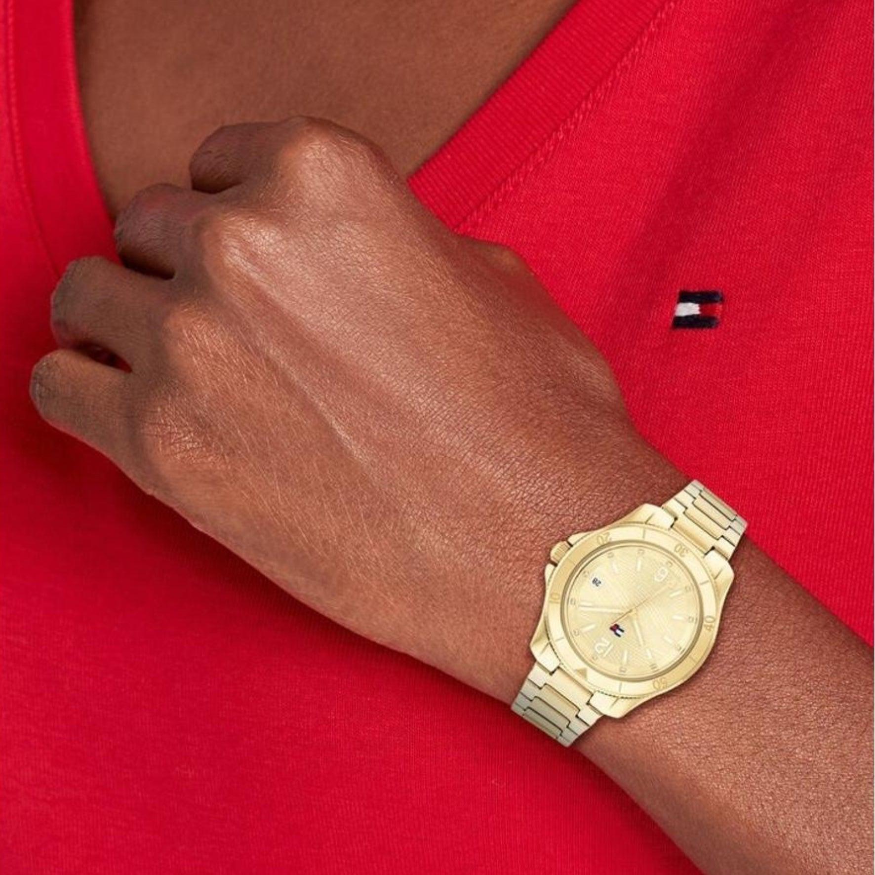 Γυναικείο ρολόι Tommy Hilfiger Brooke 1782513, με μπρασελέ σε χρυσό χρώμα από ανοξείδωτο ατσάλι και χρυσό καντράν με λειτουργία ημερομηνίας φορεμένο σε γυναικείο χέρι.