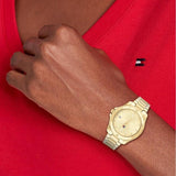 Γυναικείο ρολόι Tommy Hilfiger Brooke 1782513, με μπρασελέ σε χρυσό χρώμα από ανοξείδωτο ατσάλι και χρυσό καντράν με λειτουργία ημερομηνίας φορεμένο σε γυναικείο χέρι.