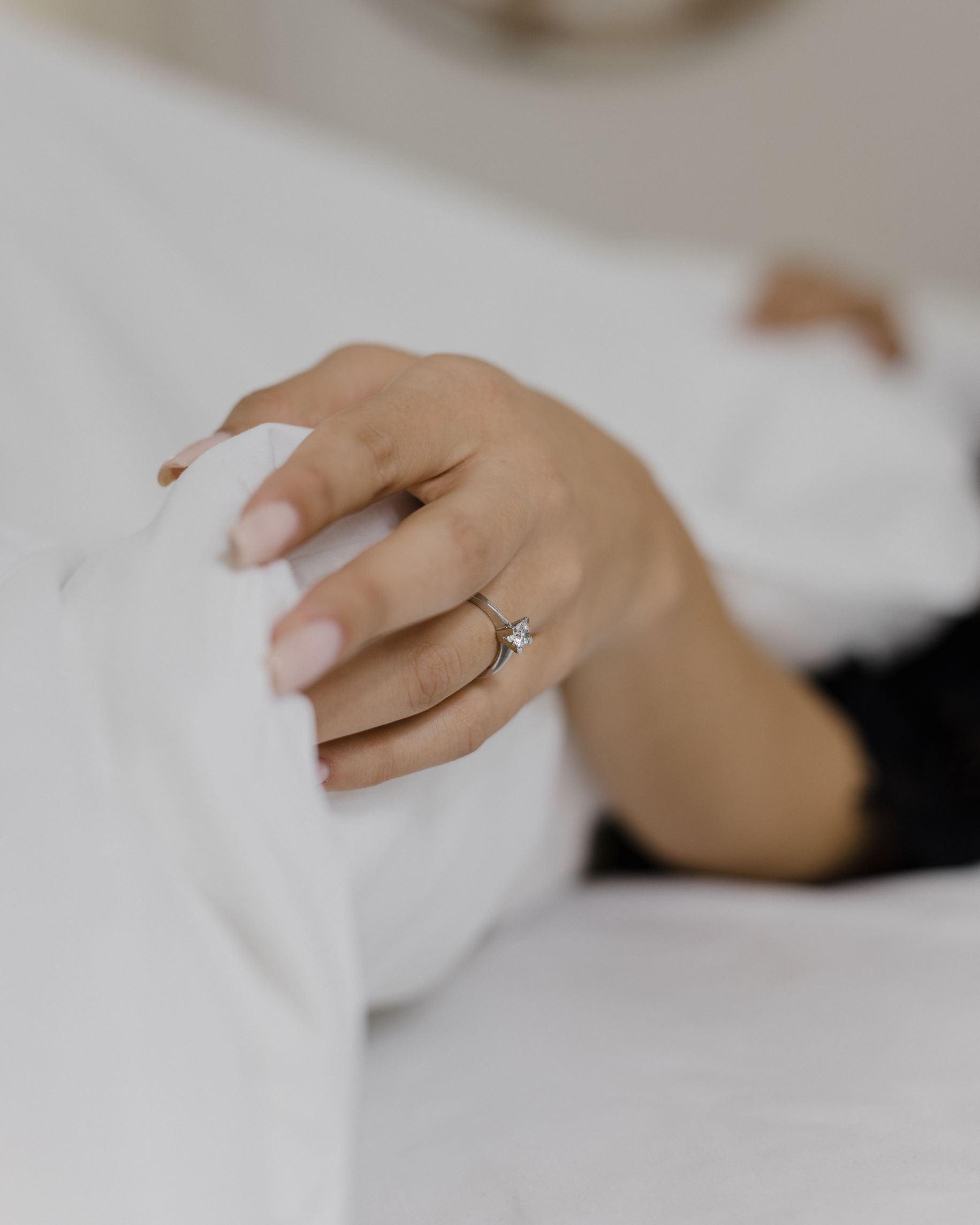 Λευκόχρυσο μονόπετρο με διαμάντι και καστόνι σχήματος V, φορεμένο σε γυναικείο χέρι.