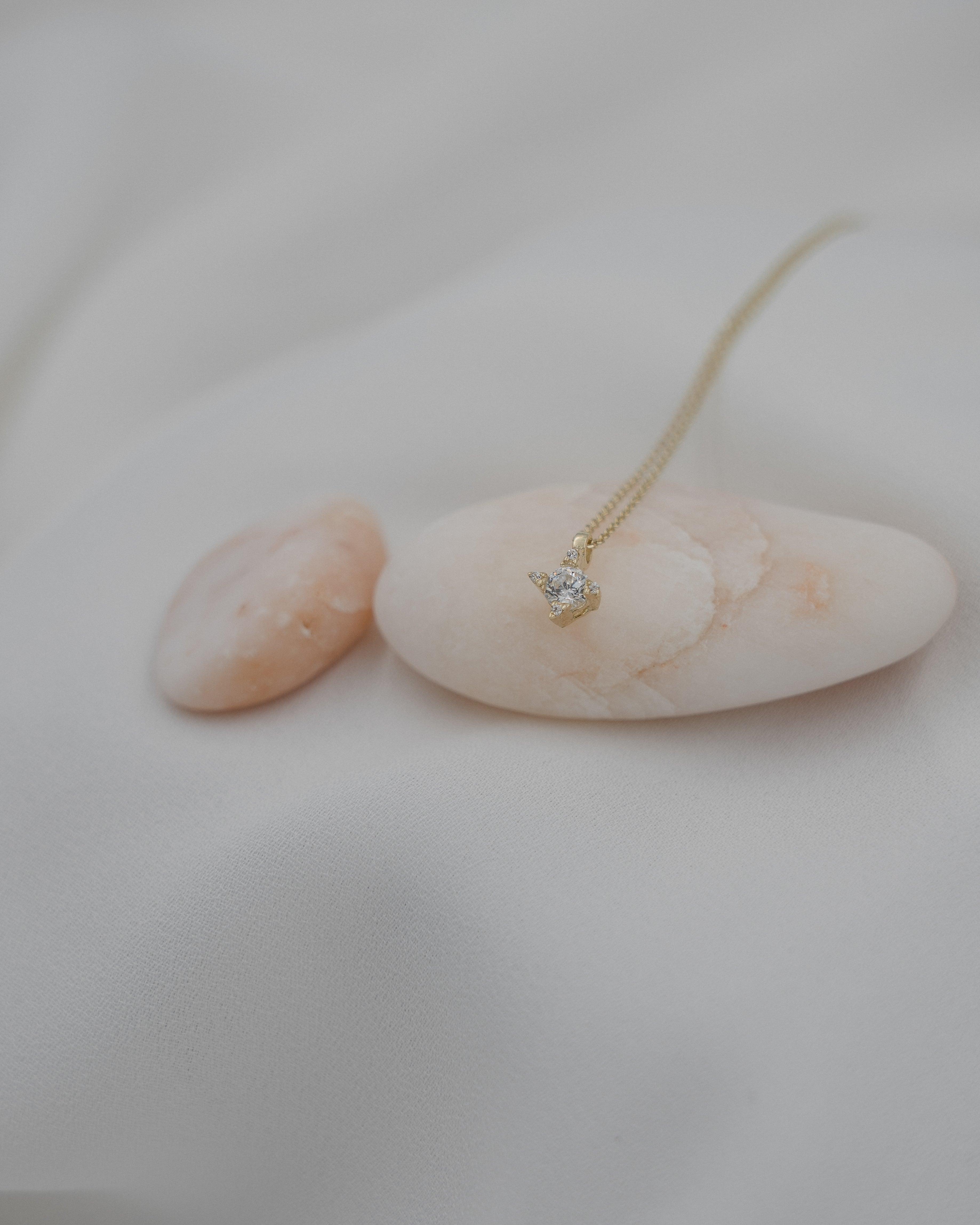 Γυναικείο χρυσό κολιέ με μονοπετράκι στο κέντρο στολισμένο με μικρά ζιργκόν περιμετρικά, σε λευκό φόντο.