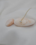 Γυναικείο χρυσό κολιέ με μονοπετράκι στο κέντρο στολισμένο με μικρά ζιργκόν περιμετρικά, σε λευκό φόντο.