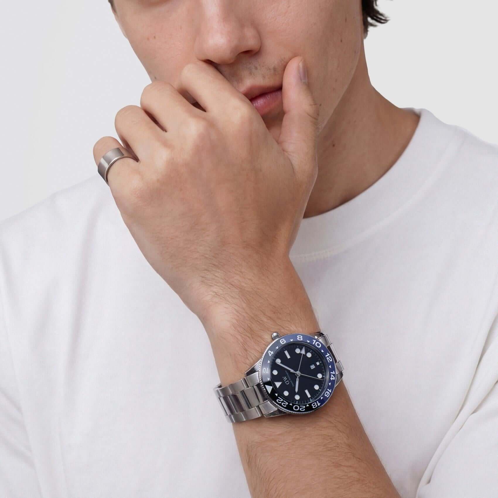 Ανδρικό ρολόι Daniel Wellington Iconic GMT DW00100921 φορεμένο με ασημί ατσάλινο μπρασελέ, μαύρο καντράν, γκρι λεπτομέρειες και μαύρη-μπλε κεραμική στεφάνη.