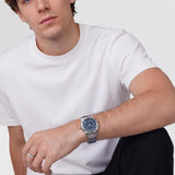 Ανδρικό ρολόι Daniel Wellington Iconic GMT DW00100922 φορεμένο με ασημί ατσάλινο μπρασελέ, μπλε καντράν, γκρι λεπτομέρειες και γκρι κεραμική στεφάνη.