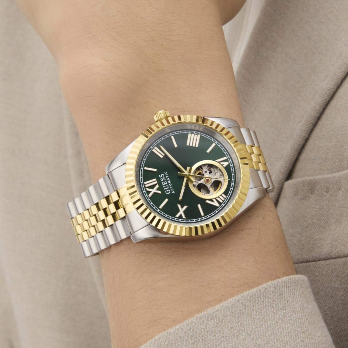 Ανδρικό ρολόι Guess Connoisseur GW0984G4 φορεμένο με δίχρωμο ατσάλινο μπρασελέ σε ασημί και χρυσό χρώμα, πράσινο skeleton καντράν και χρυσές λεπτομέρειες.
