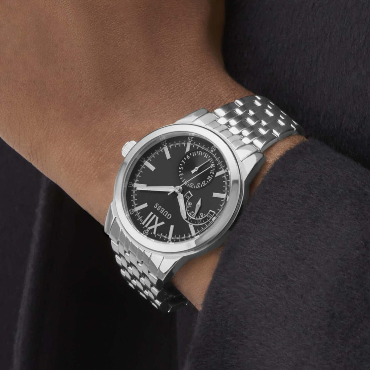 Ανδρικό ρολόι Guess Emerson GW0976G1 φορεμένο με ασημί ατσάλινο μπρασελέ, μαύρο καντράν και ασημί λεπτομέρειες.