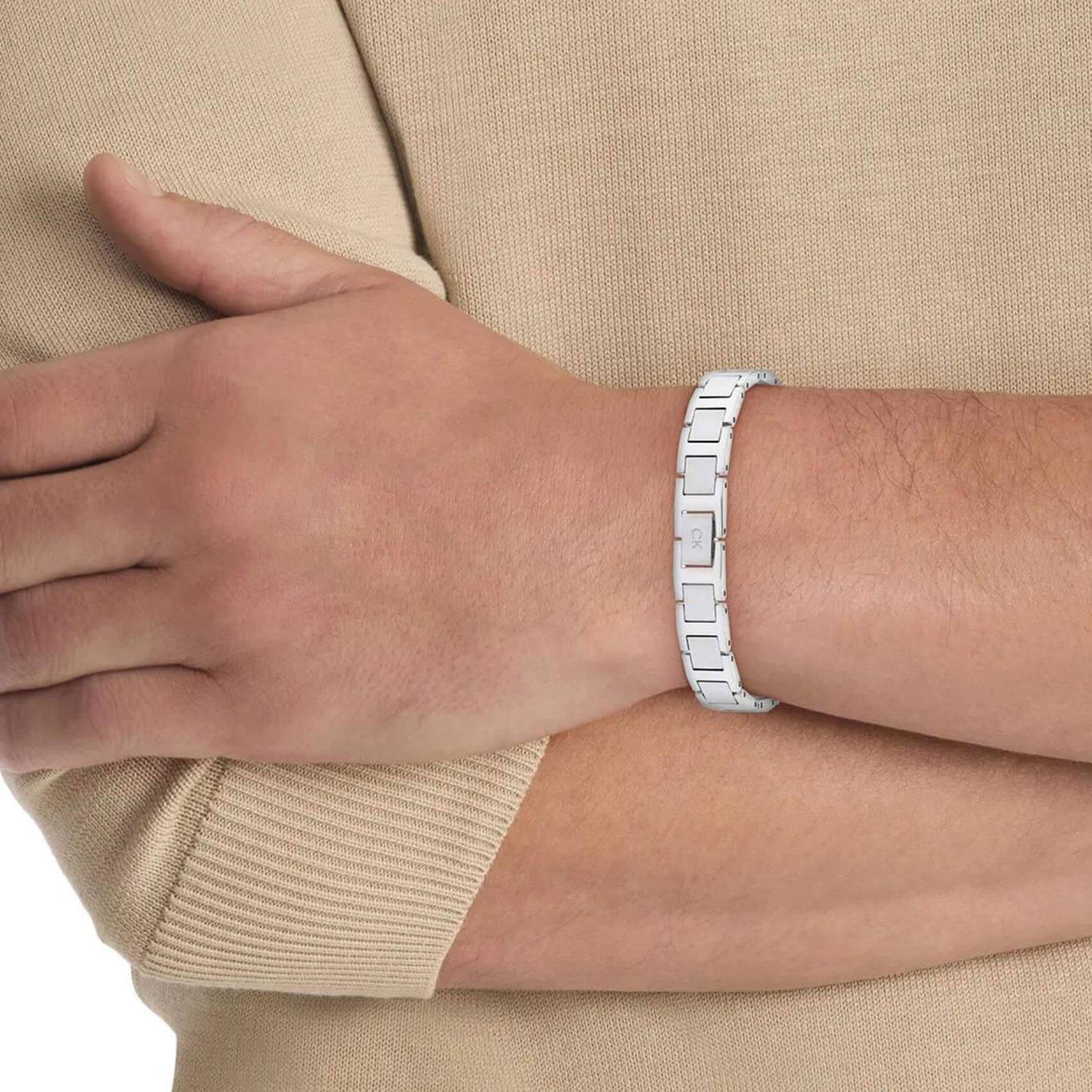 Μοντέλο φορά το ανδρικό ατσάλινο βραχιόλι Calvin Klein 35100008 με σχέδιο μπρασελέ σε ασημί χρώμα