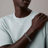Ανδρικό βραχιόλι Calvin Klein 35100040 μακραμέ κατασκευασμένο από ατσάλι σε ασημί χρώμα με σχέδιο μπρασελέ και μαύρο κορδόνι, φορεμένο.