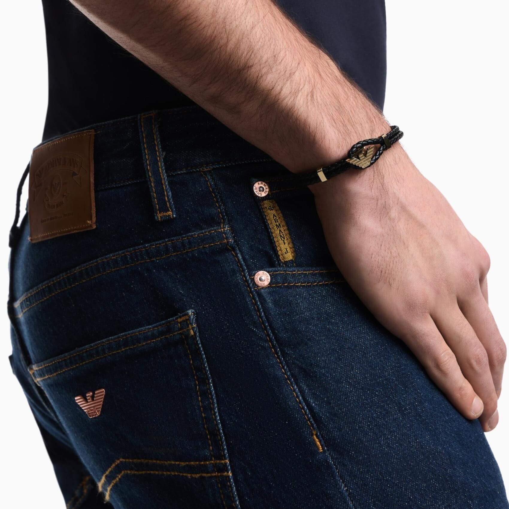 Ανδρικό βραχιόλι Emporio Armani Eagle Logo EGS3321710 φορεμένο στον καρπό, με μαύρο δερμάτινο λουράκι και χρυσό μοτίφ λογότυπο.