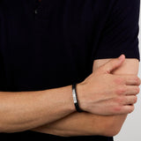 Ανδρικό βραχιόλι Maserati JM525AVE29 φορεμένο σε ανδρικό χέρι, από ανακυκλωμένο μαύρο δέρμα με ασημί ατσάλινο στοιχείο και μαύρη τρίαινα.