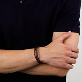 Bραχιόλι Maserati JM525AVE33 φορεμένο σε ανδρικό χέρι, με καφέ τριπλό δερμάτινο λουράκι και ασημί ατσάλινο στοιχείο με ροζ χρυσή τρίαινα.