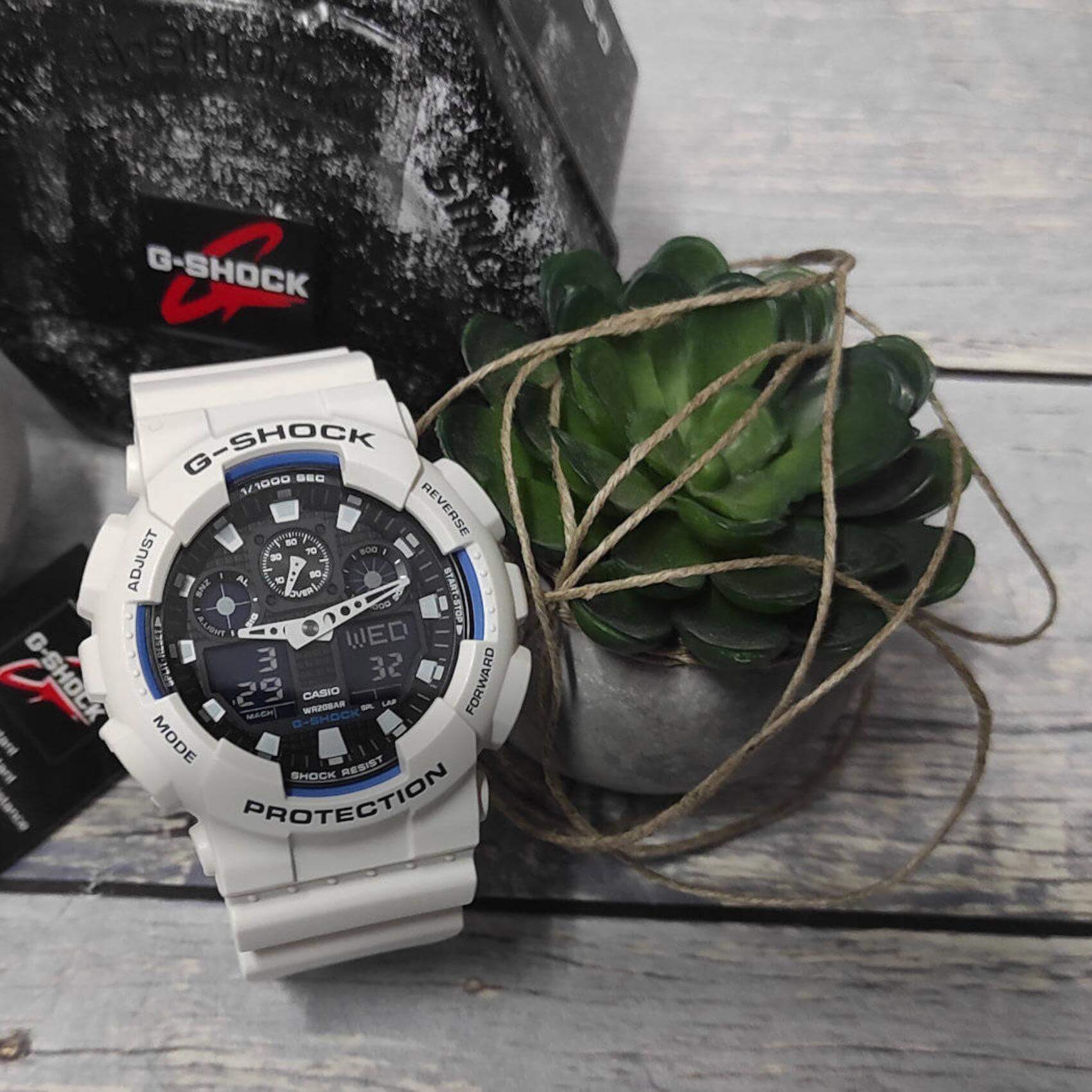 Καταδυτικό ρολόι χρονογράφος Casio G-Shock GA-100B-7AER με λευκό καουτσούκ λουράκι, μαύρο καντράν με μπλε λεπτομέρειες και στεγανότητα 20ATM-200Μ.