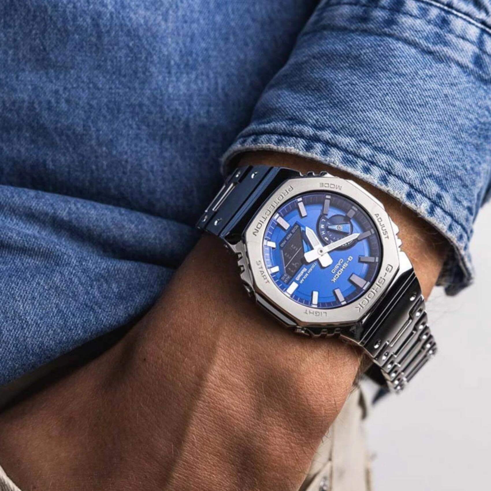 Ανδρικό ρολόι Casio G-SHOCK GM-B2100AD-2AER φορεμένο στον καρπό με ασημί ατσάλινο μπρασελέ και μπλε καντράν.
