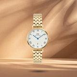 Γυναικείο ρολόι Daniel Wellington Petite Roman Numerals DW00100857 με χρυσό μπρασελέ από ανοξείδωτο ατσάλι και λευκό καντράν διαμέτρου 28mm με μπλε δείκτες.