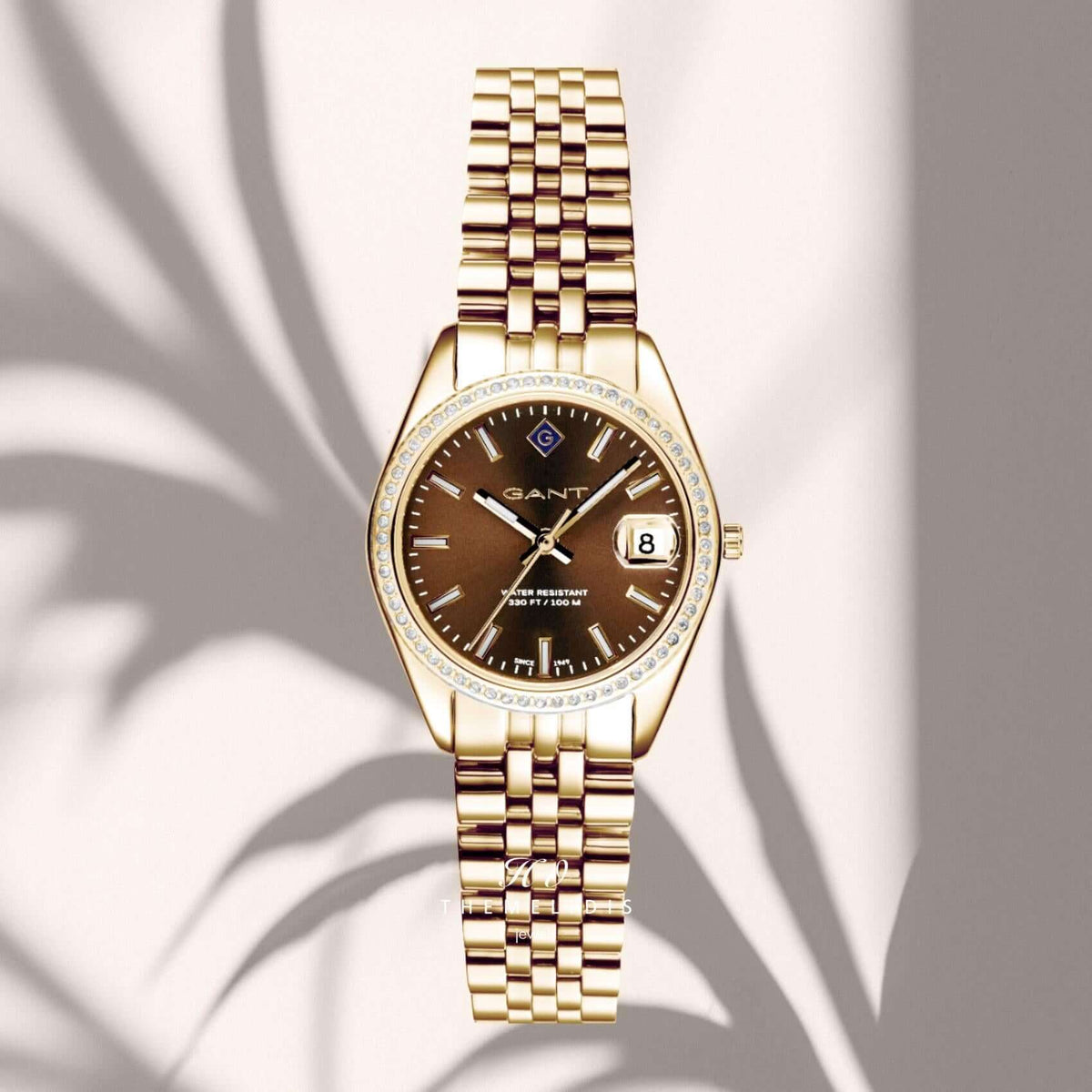 Γυναικείο ρολόι Gant Sussex Mini Bijou G181103 με χρυσό μπρασελέ και καφέ καντράν 28mm με ζιργκόν, σε μπεζ φόντο.
