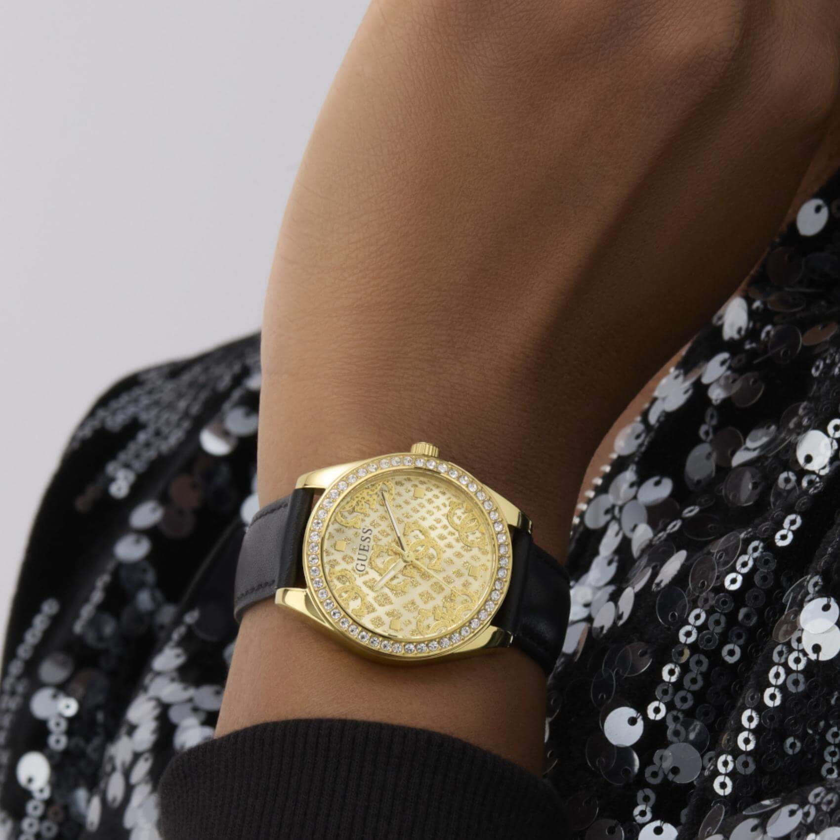 Γυναικείο ρολόι Guess Boa GW0989L2 φορεμένο με μαύρο δερμάτινο λουράκι, χρυσό καντράν και λαμπερά ζιργκόν.
