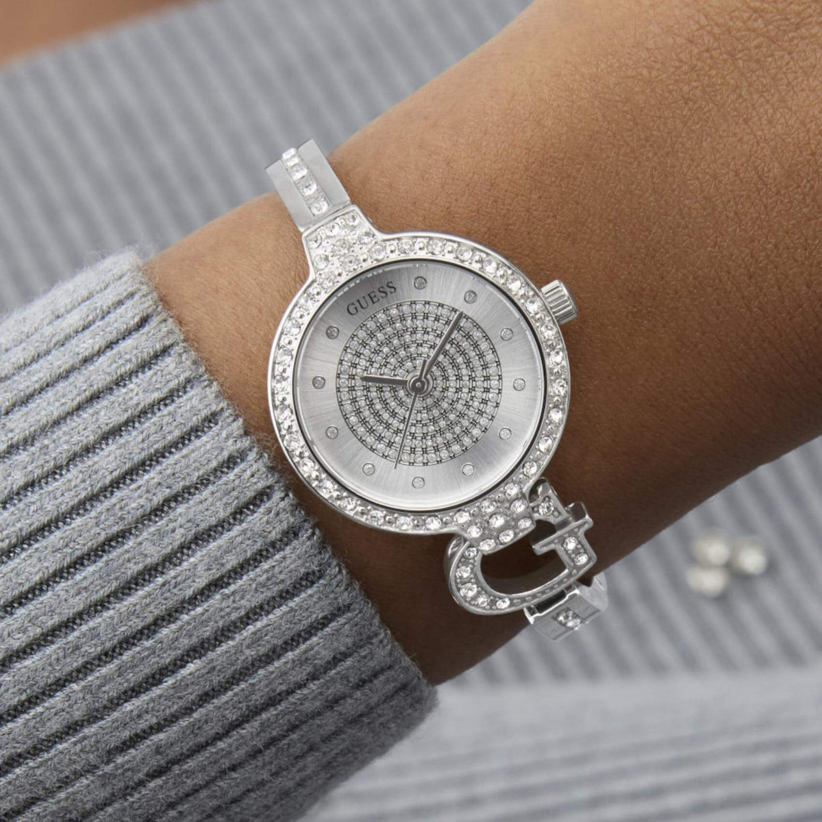 Γυναικείο ρολόι Guess Giselle GW0929L1 φορεμένο με ασημί ατσάλινο μπρασελέ σε στυλ βραχιολιού, ασημί καντράν και στεφάνη με ζιργκόν.