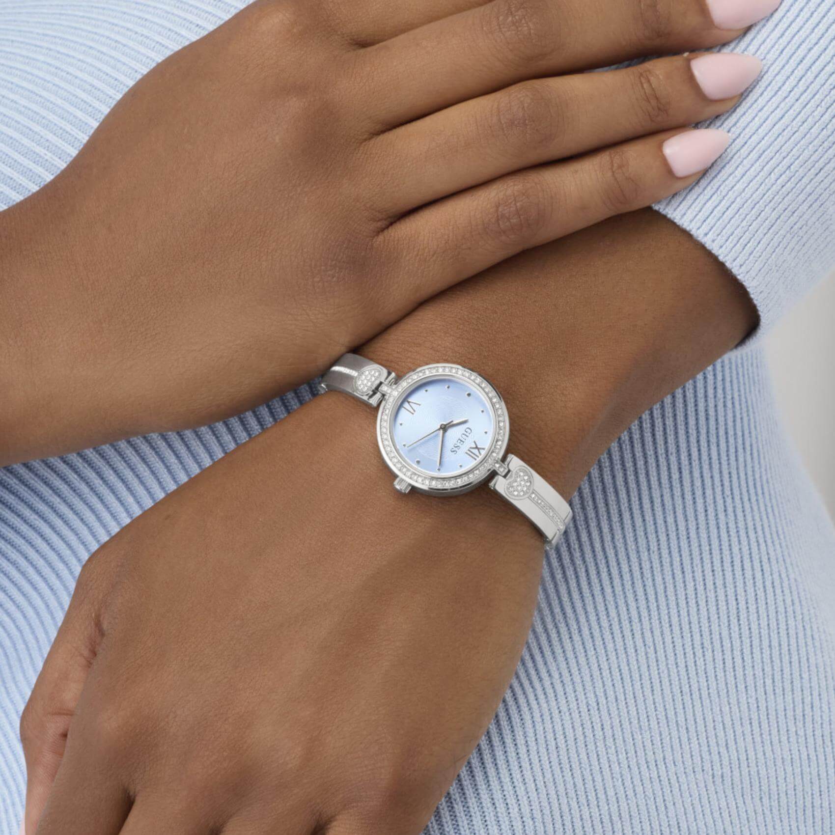 Γυναικείο ρολόι Guess Lovey GW0655L4 φορεμένο με ασημί μπρασελέ, γαλάζιο καντράν και διακόσμηση με ζιργκόν.