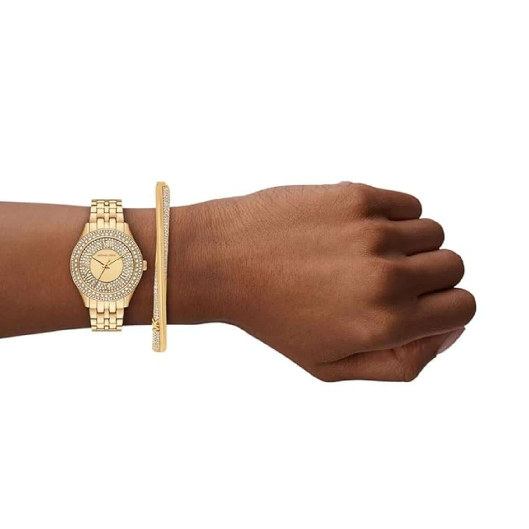 Φωτογραφία του γυναικείου ρολογιού Michael Kors Harlowe MK4974 φορεμένο σε μοντέλο, αναδεικνύοντας το χρυσό μπρασελέ και το καντράν με ζιργκόν σε συνδυασμό με το βραχιόλι