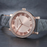 Γυναικείο ρολόι Michael Kors Norie MK2619 με γκρι δερμάτινο λουράκι, στρογγυλό ροζ χρυσό καντράν και στεφάνι 38mm με ζιργκόν.