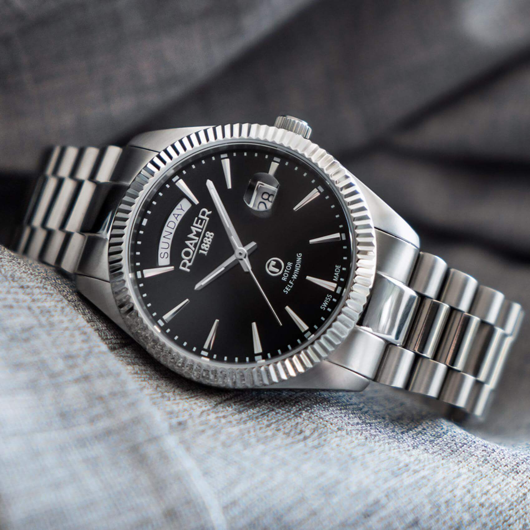 Αυτόματο ρολόι open back Roamer Primeline Day Date 981662-41-55-90 με ασημί μπρασελέ, μαύρο καντράν με ένδειξη ημέρας και ημερομηνίας και κάσα διαμέτρου 42mm.