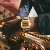 Ψηφιακό ρολόι Casio G-SHOCK GM-5600YMG-9ER με χρυσό καουτσούκ λουράκι και χρυσό τετράγωνο καντράν 49.6×43.2mm-φορεμένο.