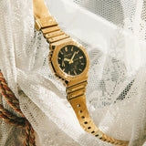 Ρολόι Casio G-Shock GM-2100YMG-9AER με χρυσό καουτσούκ λουράκι και οκτάγωνο μαύρο καντράν 45,4mm. με ημερομηνία-σε λευκό ύφασμα.