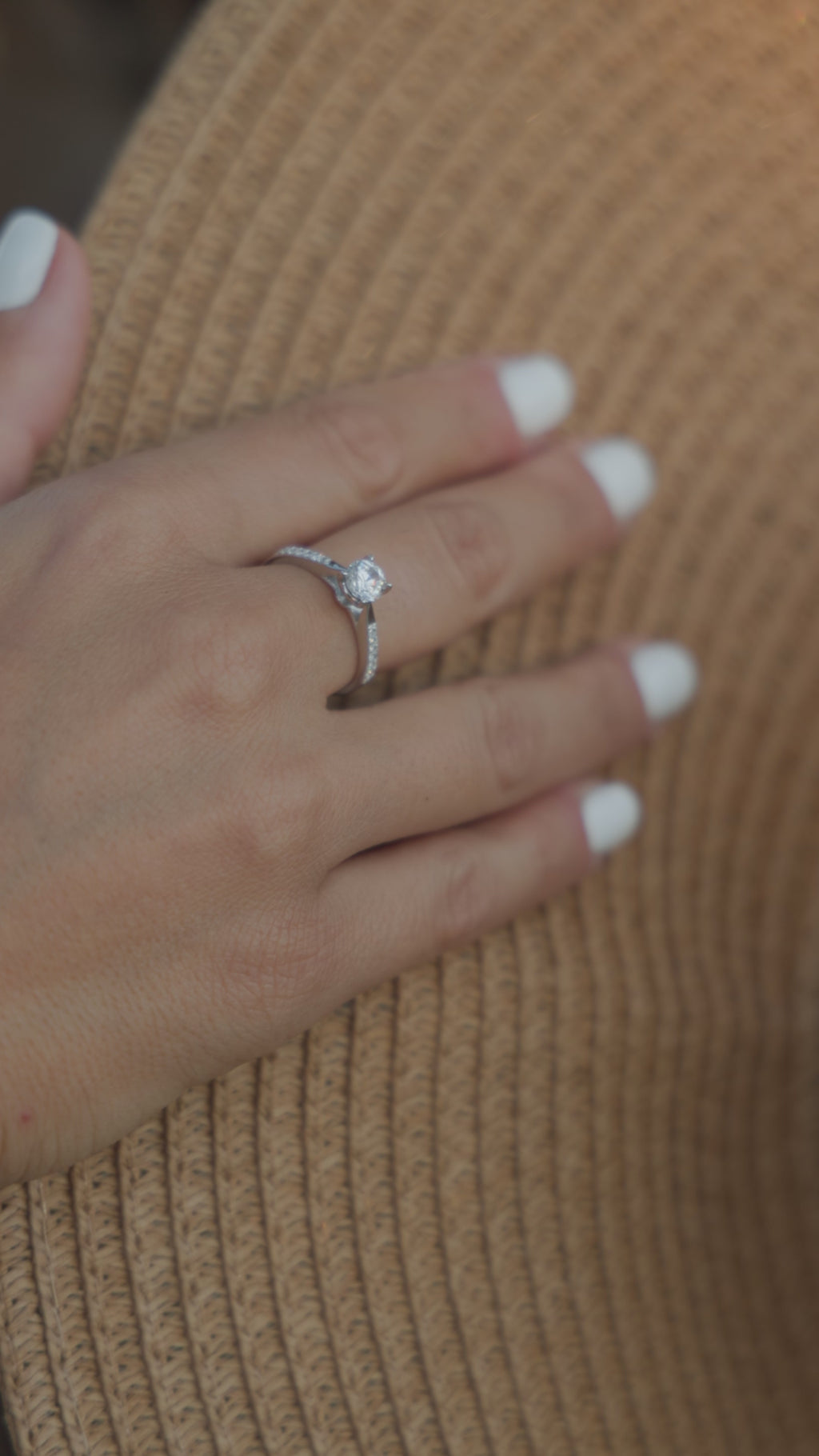 Μονόπετρο δαχτυλίδι με διαμάντι κατασκευασμένο από λευκόχρυσο, με πλαϊνές πέτρες από μικρότερα διαμάντια, φορεμένο σε γυναικείο χέρι.