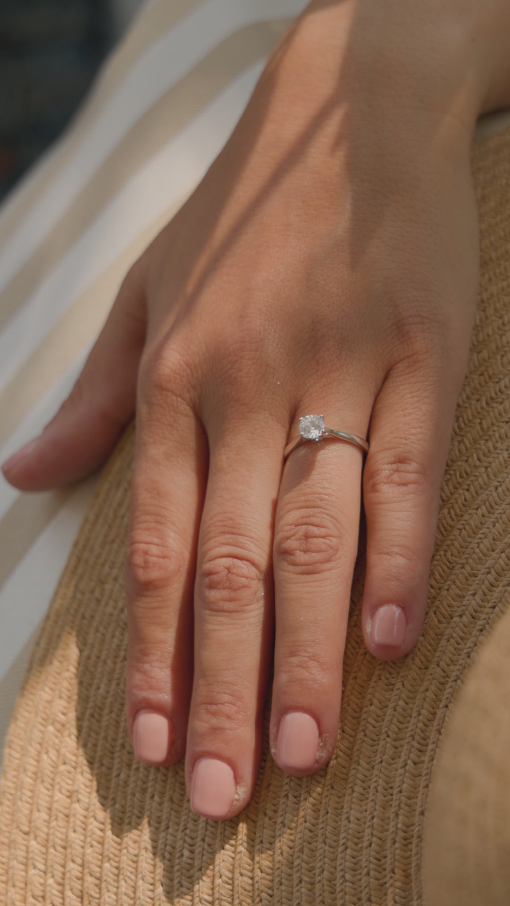 Λευκόχρυσο μονόπετρο δαχτυλίδι με διαμάντι και καστόνι που αγκαλιάζει την πέτρα με τέσσερα δόντια, φορεμένο σε γυναικείο χέρι.