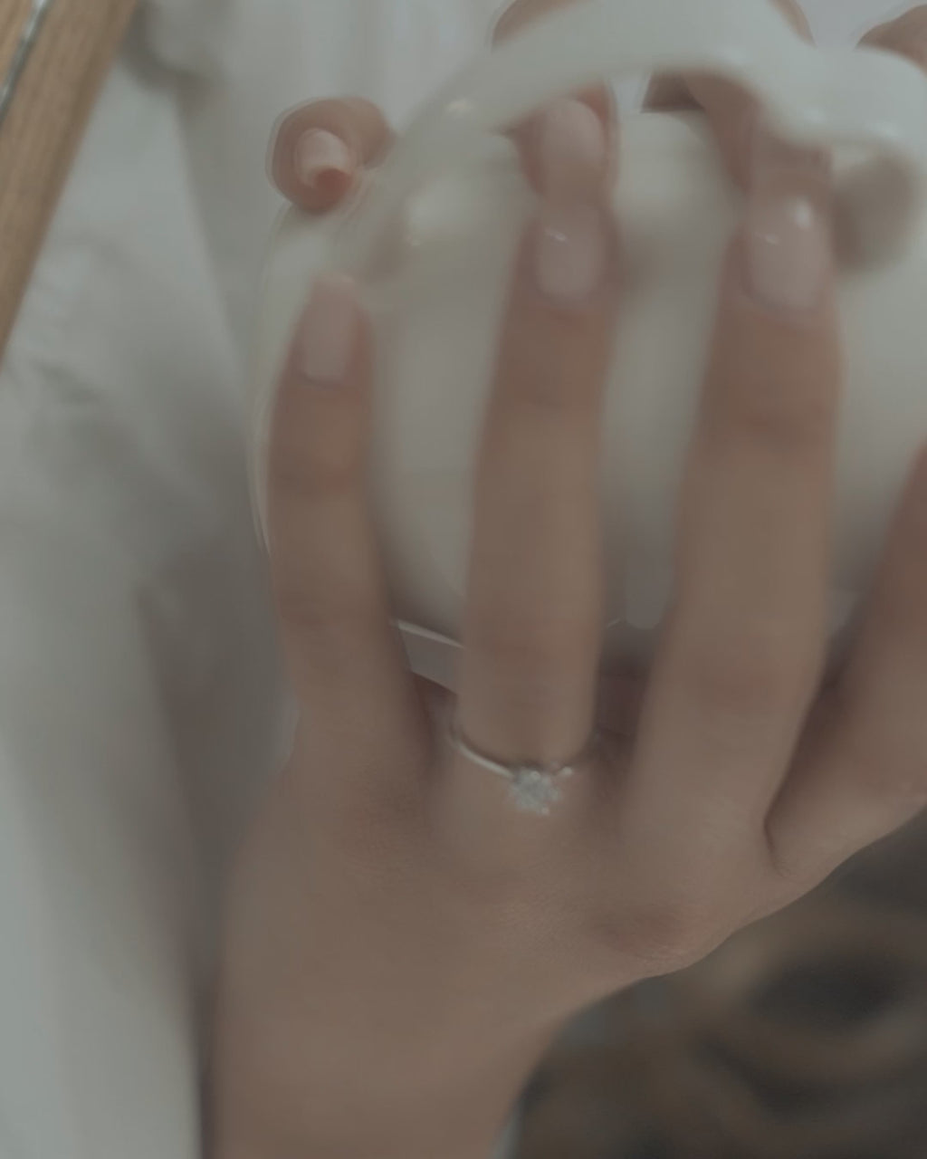 Μονόπετρο δαχτυλίδι γάμου με κεντρικό διαμάντι και πέτρες brilliant περιμετρικά κατασκευασμένο από λευκόχρυσο, φορεμένο σε γυναικέιο χέρι.