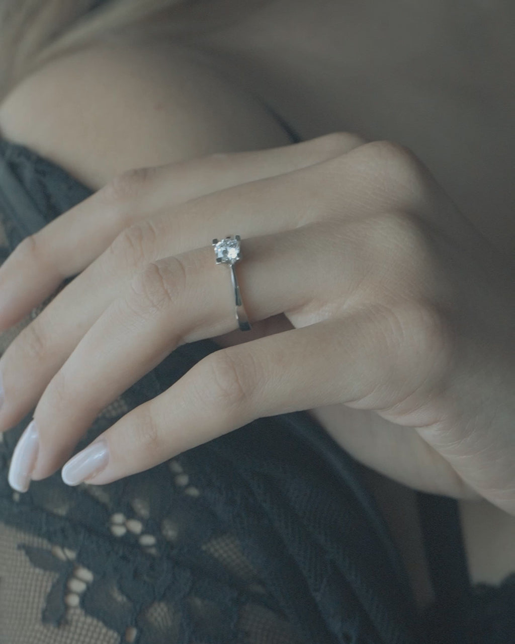 Λευκόχρυσο μονόπετρο με διαμάντι και καστόνι σχήματος V, φορεμένο σε γυναικείο χέρι.