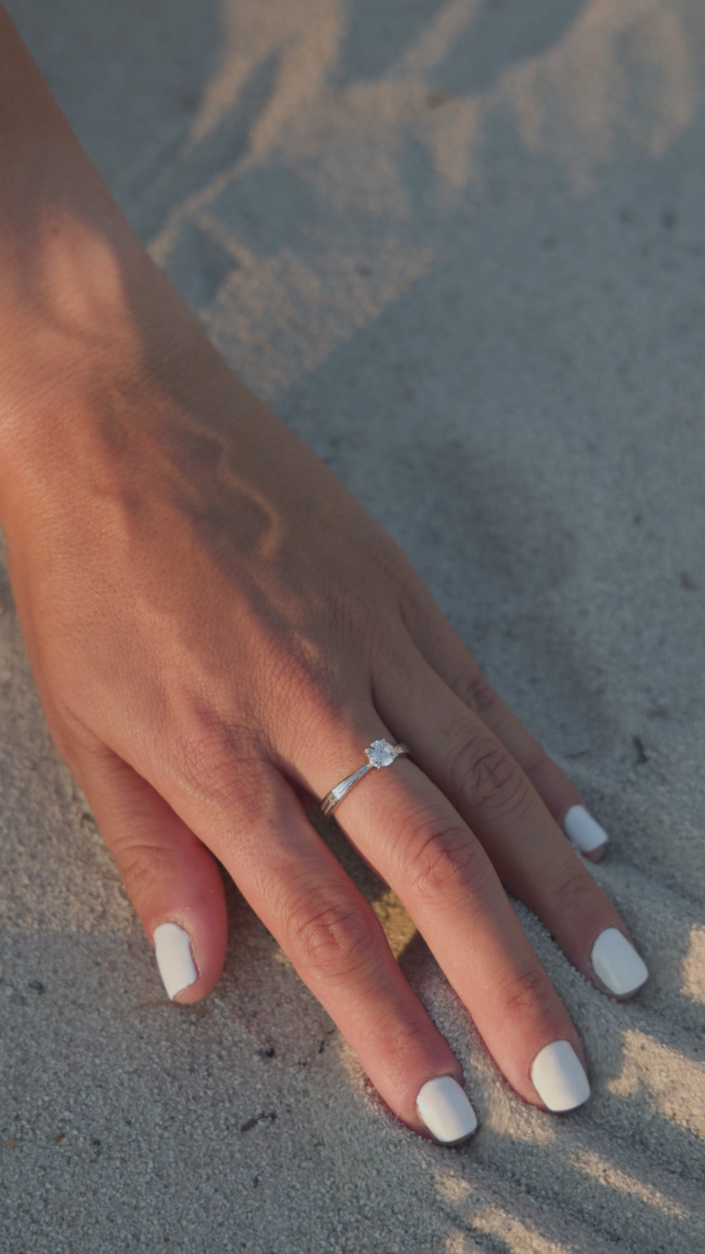 Μονόπετρο δαχτυλίδι με διαμάντι κατασκευασμένο από λευκόχρυσο και καστόνι σε σχήμα "V", φορεμένο σε γυναικείο χέρι.