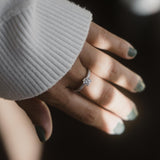 ικό διαμάντι round cut, πλαίνές πέτρες από μικρότερα διαμάντια και καστόνι σε σχήμα "V", κατασκευασμένο από λευκόχρυσο φορεμένο σε γυναικείο χέρι.