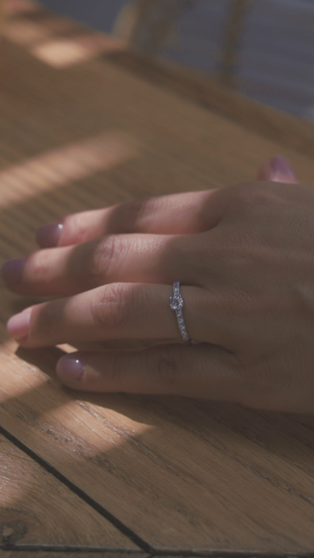 Μονόπετρο δαχτυλίδι με διαμάντι, κατασκευασμένο από λευκόχρυσο. πλαϊνές πέτρες από μικρότερα διαμάντια και καστόνι με τέσσερα δόντια, φορεμένο σε γυναικείο χέρι.