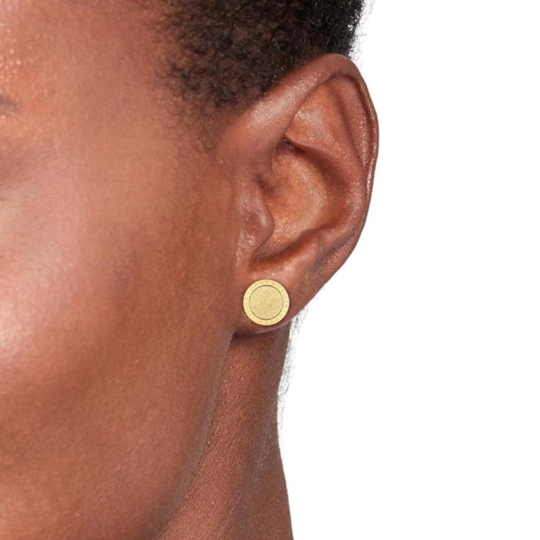 Γυναικεία σκουλαρίκια καρφωτά Tommy Hilfiger με στρογγυλό σχέδιο σε χρυσό χρώμα, φορεμένα σε γυναικείο αυτί.