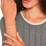 Γυναικείο βραχιόλι σε χρυσό χρώμα και κρεμαστό στοιχείο από λευκό φίλντισι της Tommy Hilfiger, φορεμένο σε γυναικείο χέρι.