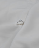Λευκόχρυσο μονόπετρο δαχτυλίδι με διαμάντι και καστόνι σε σχήμα φλόγας, επάνω σε λευκό μετάξι.