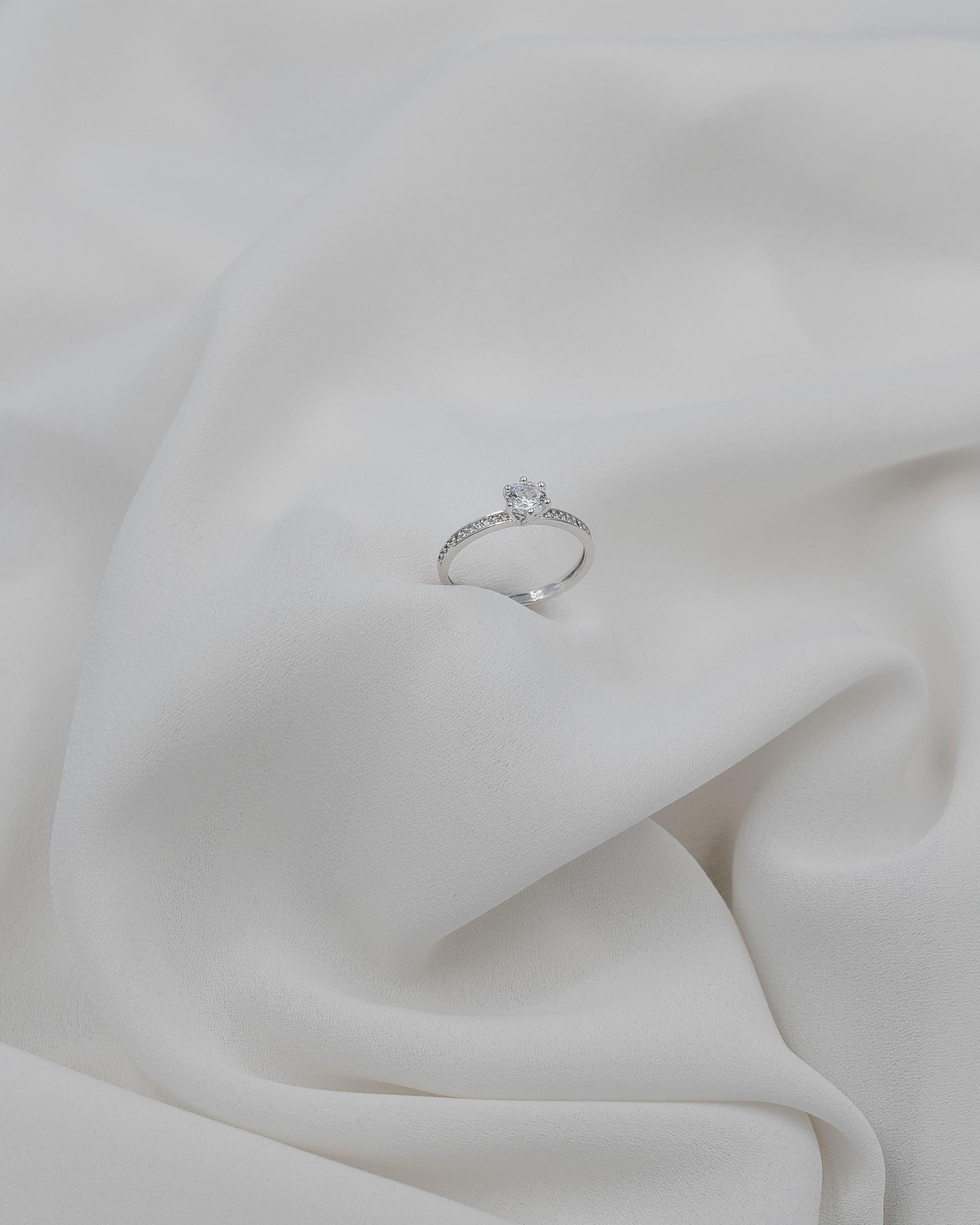 Λευκόχρυσο μονόπετρο με διαμάντι, διακοσμημένο με πλαϊνές πέτρες σε λευκό πέπλο.