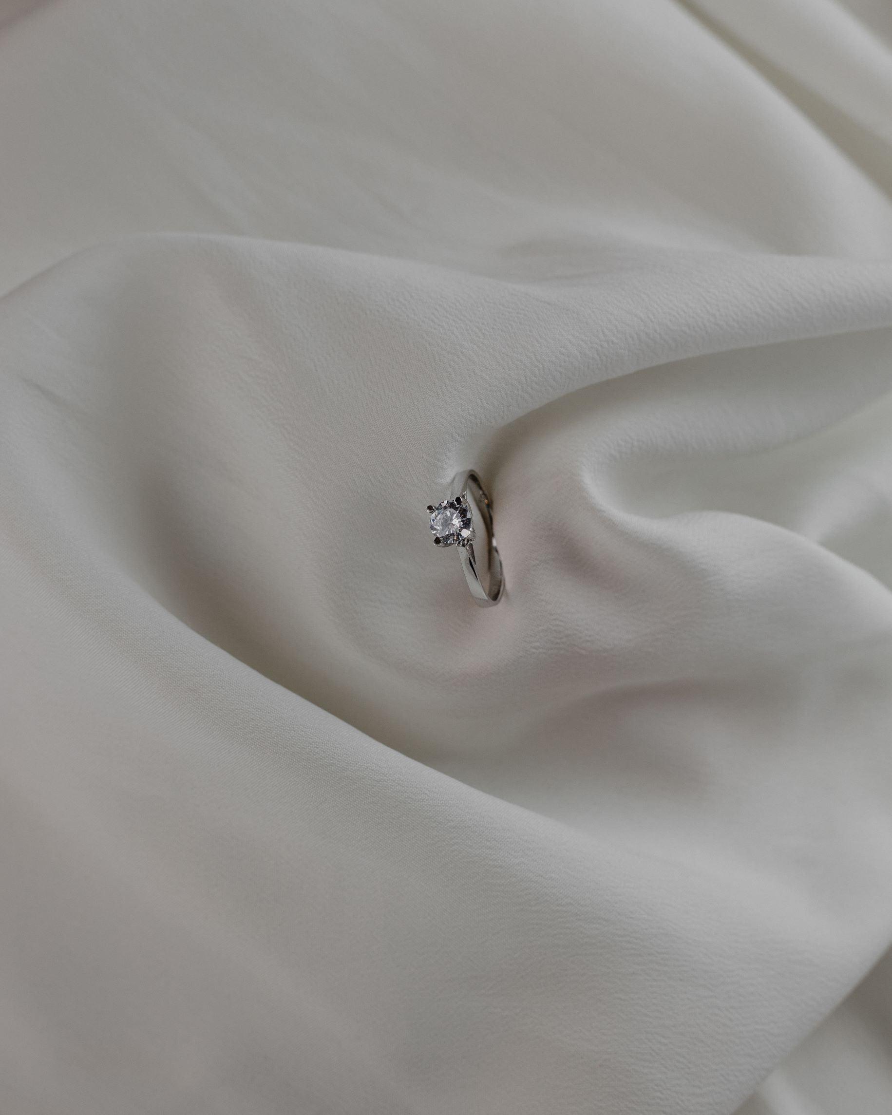 Λευκόχρυσο μονόπετρο με διαμάντι και καστόνι σε σχήμα "V" σε λευκό ύφασμα.