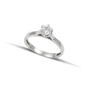 Λευκόχρυσο μονόπετρο δαχτυλίδι με διαμάντι και καστόνι με έξι δόντια, φορεμένο σε γυναικείο χέρι.
