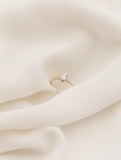 Μονόπετρο δαχτυλίδι με διαμάντι κατασκευασμένο από λευκόχρυσο με ανάγλυφες λεπτομέρειες στα πλαίνά μέρη του δαχτυλιδιού και καστόνι με τέσσερα δόντια επάνω σε λευκό ύφασμα. 