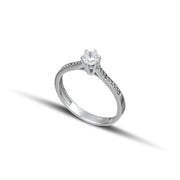 Μονόπετρο δαχτυλίδι γάμου με διαμάντι και πλαϊνές πέτρες brilliant κατασκευασμένο από λευκόχρυσο, επάνω σε λευκό βότσαλο.